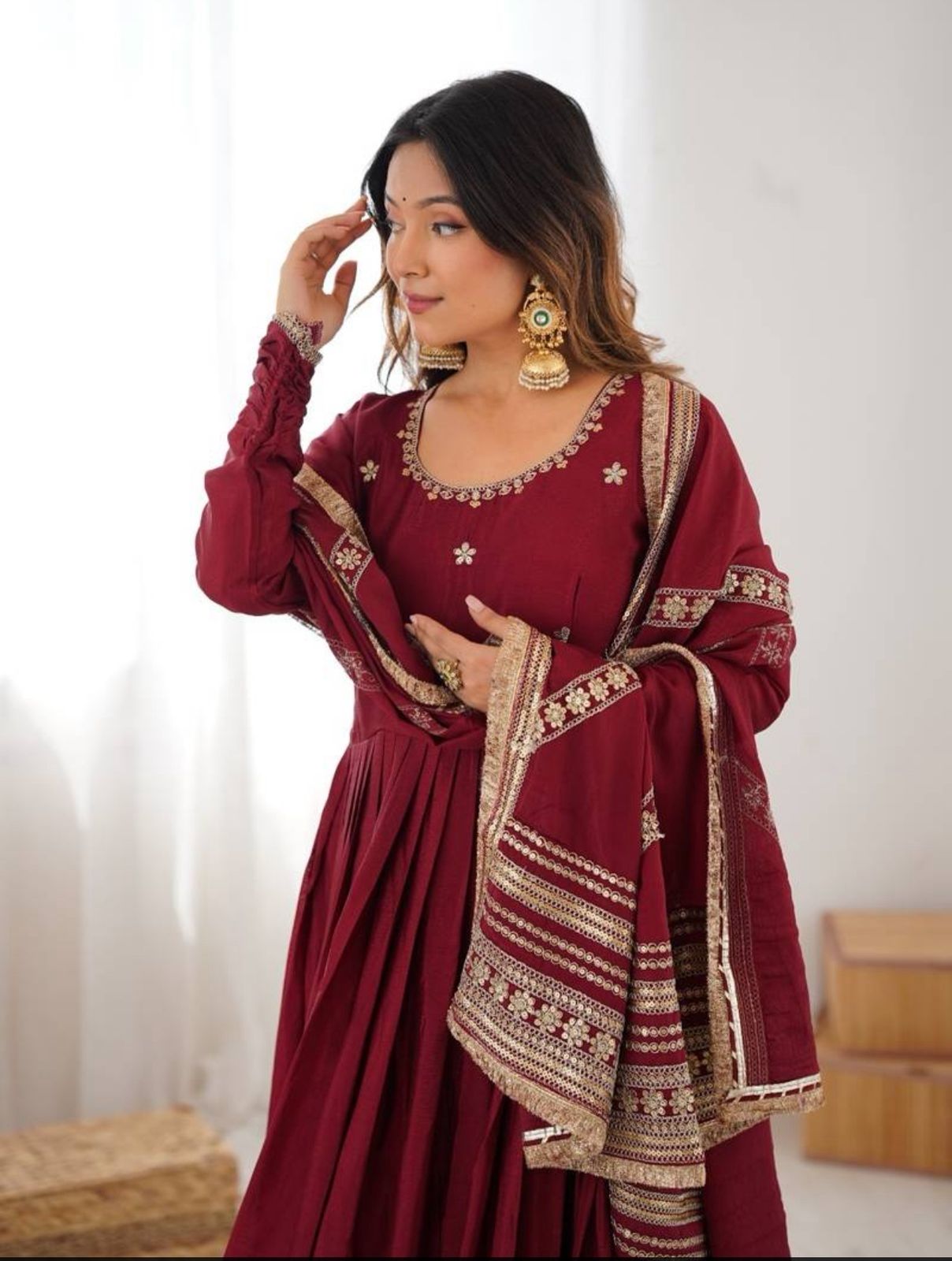 Woman wearing a traditional maroon dress with gold embroidery against a white background