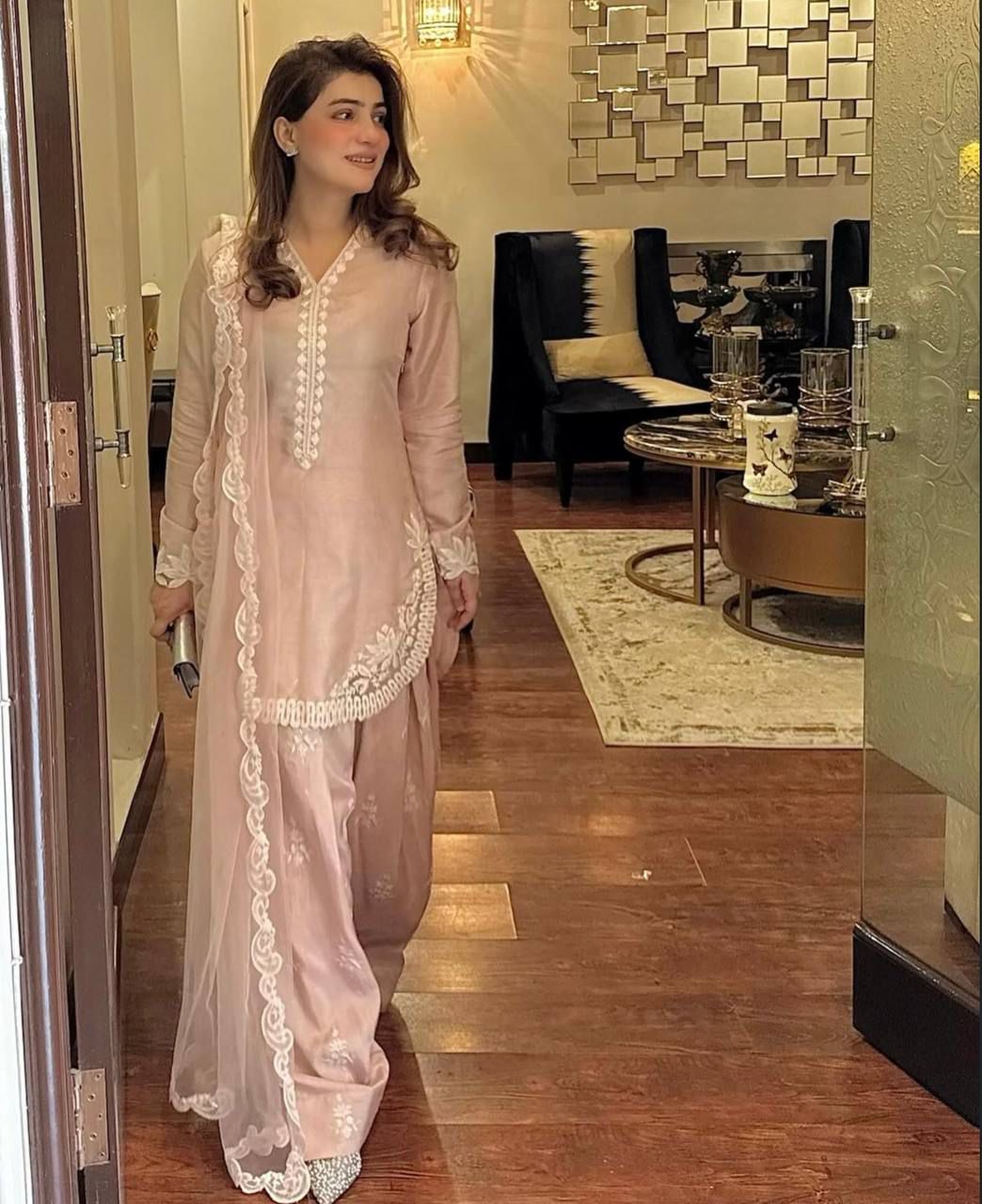Woman in a light pink traditional outfit walking through a modern interior.