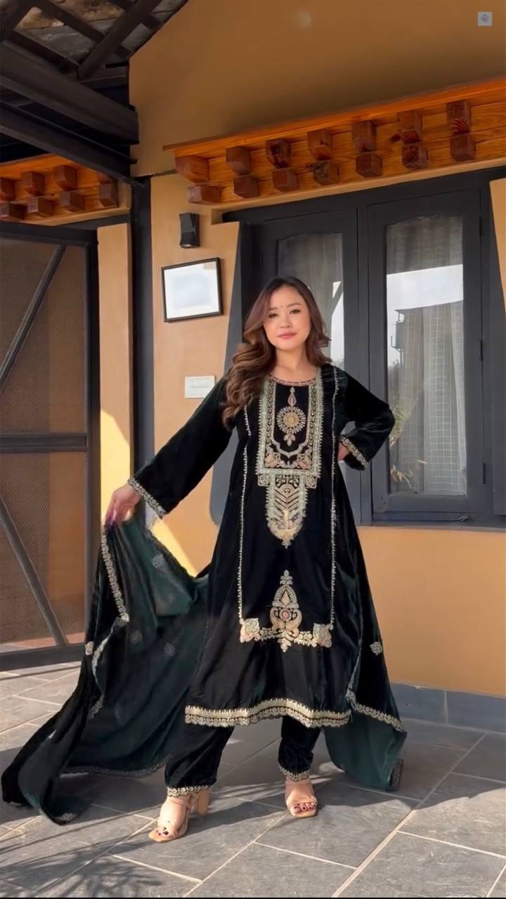 Woman wearing a green embroidered outfit standing in front of a building entrance.