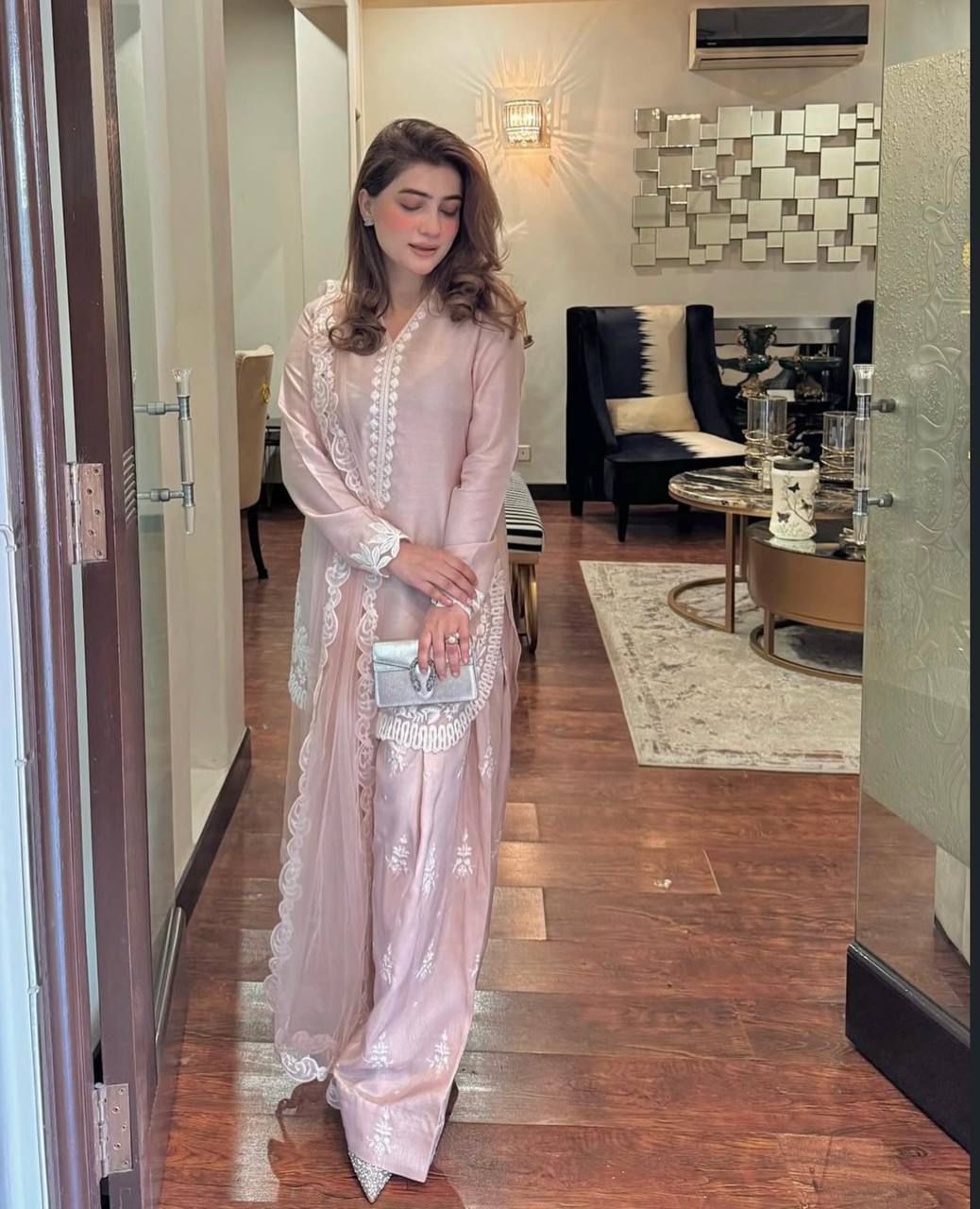 Woman in a light pink traditional outfit standing in a modern interior setting.
