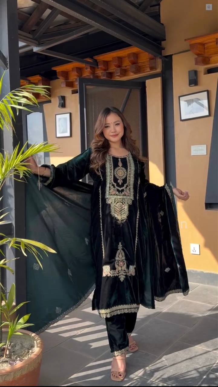 Woman in a green embroidered outfit standing in front of a building entrance.
