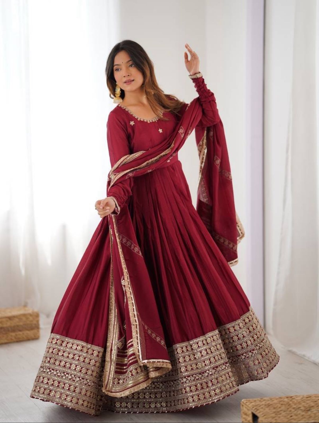 Woman wearing a maroon traditional outfit with gold embroidery against a white background