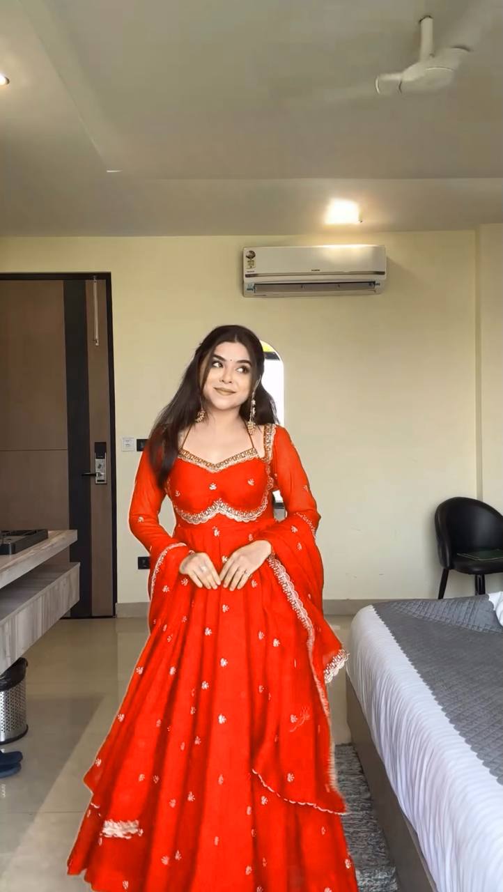 Woman in a red traditional outfit standing in a room with a bed and air conditioner.