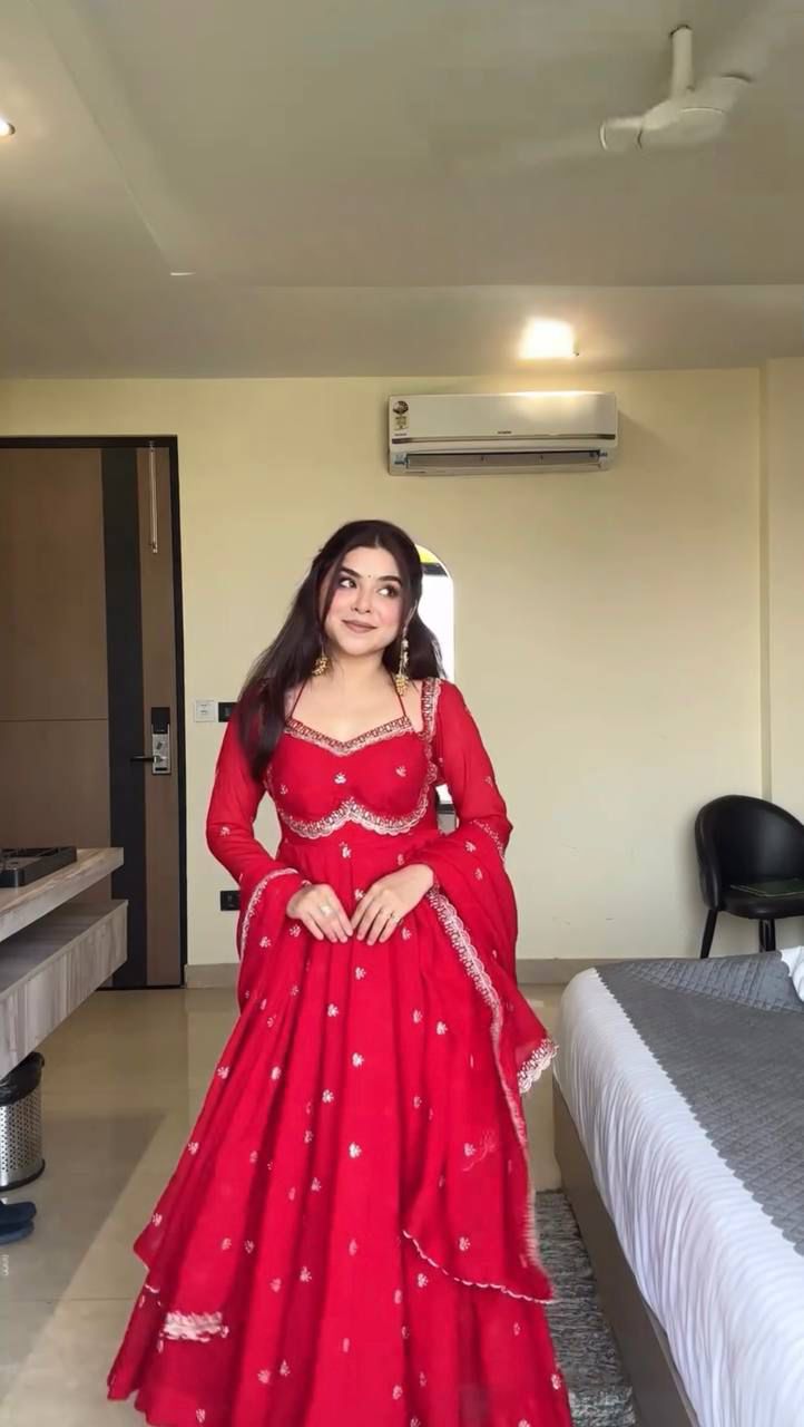 Woman in a red traditional outfit standing in a room with a bed and air conditioner.