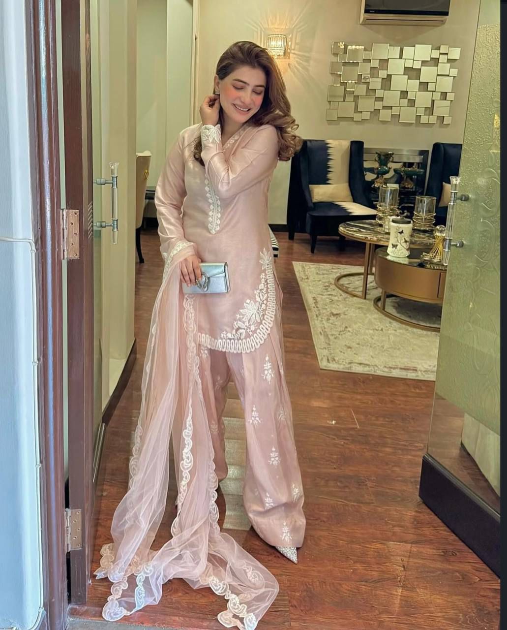 Woman in a light pink traditional outfit with white embroidery in a room.