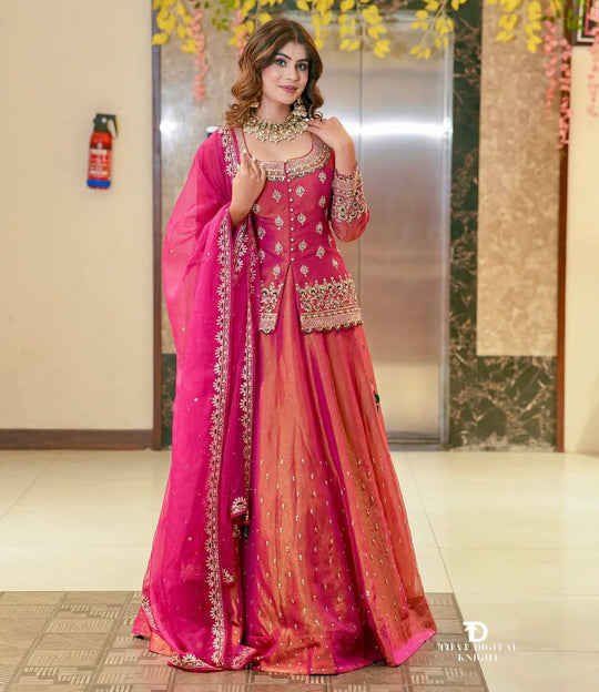 Woman in a pink traditional outfit with intricate designs in an indoor setting.