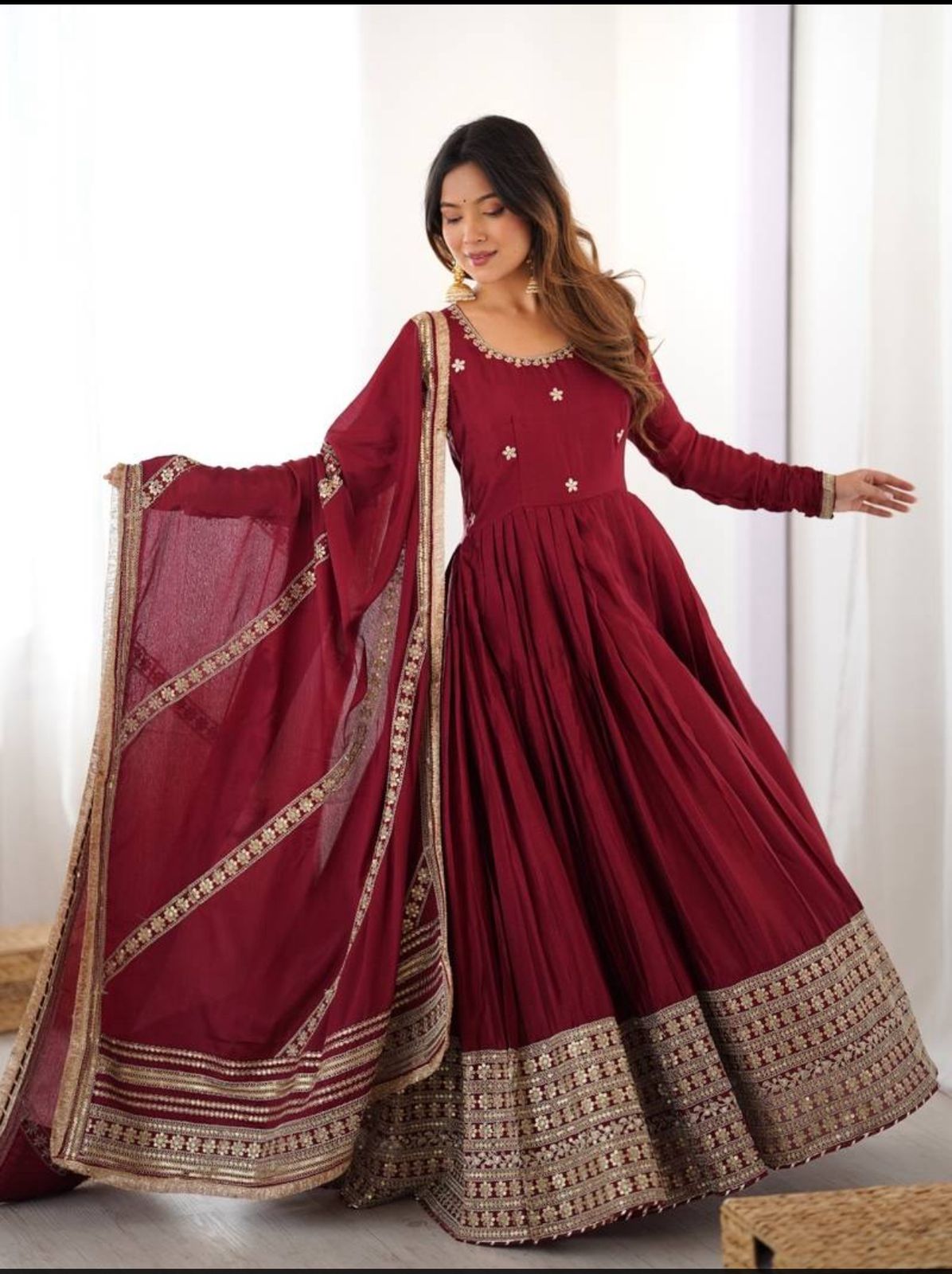 Woman wearing a maroon traditional outfit with gold embroidery against a white background